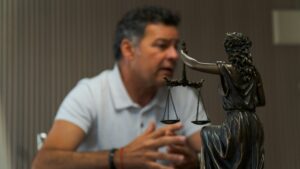 Man in a white shirt beside a statue of Lady Justice, with scales of justice between them, suggesting a legal discussion.