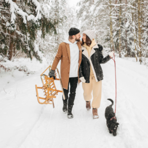 couple walking in the snow with dog on the right of the lady