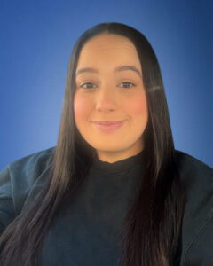 Portrait of a smiling woman with long dark hair against a solid blue background.