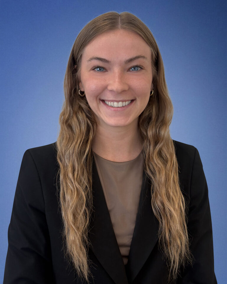 Smiling woman portrait with long wavy hair, wearing a black blazer against a blue background.