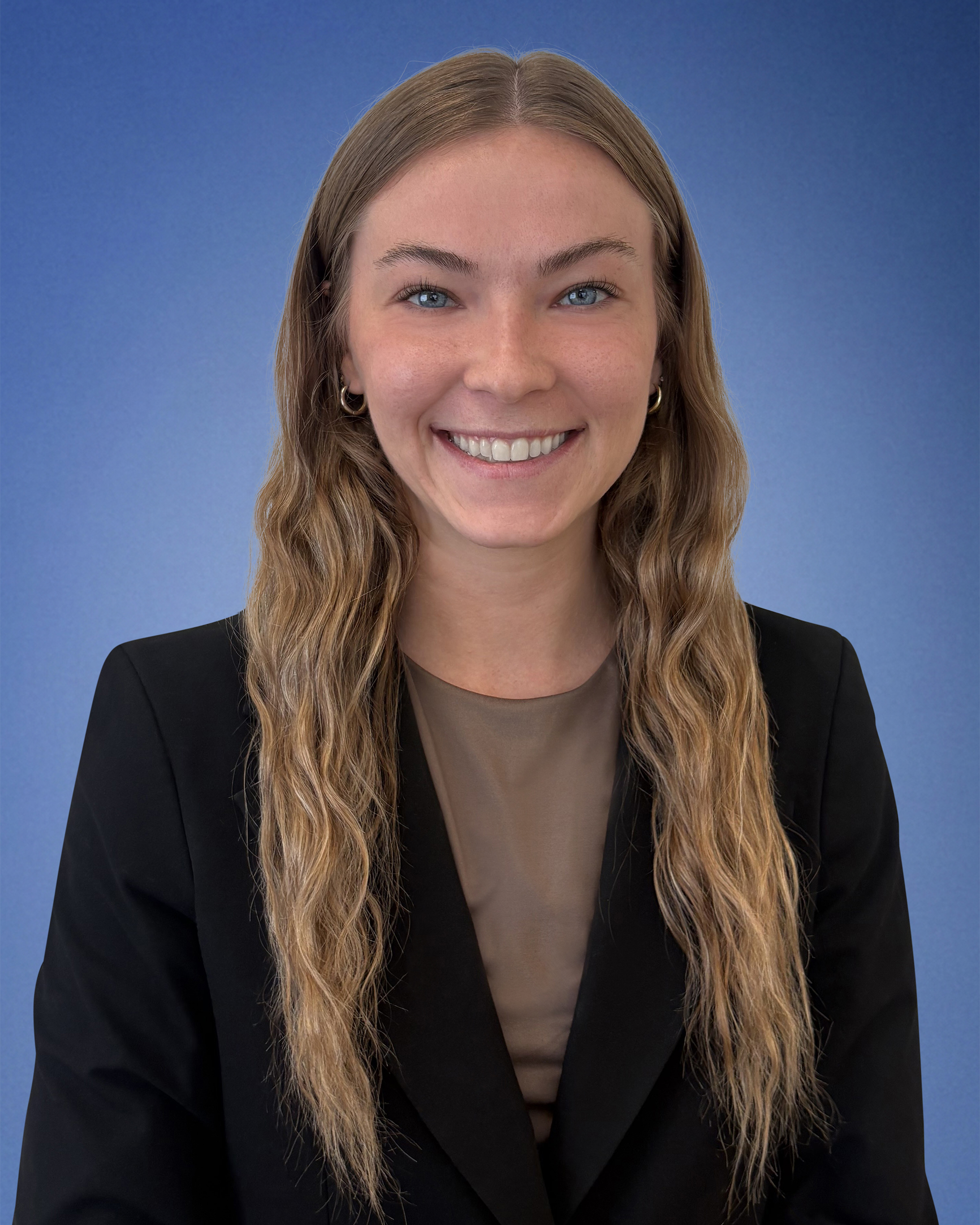 Smiling woman portrait with long wavy hair, wearing a black blazer against a blue background.