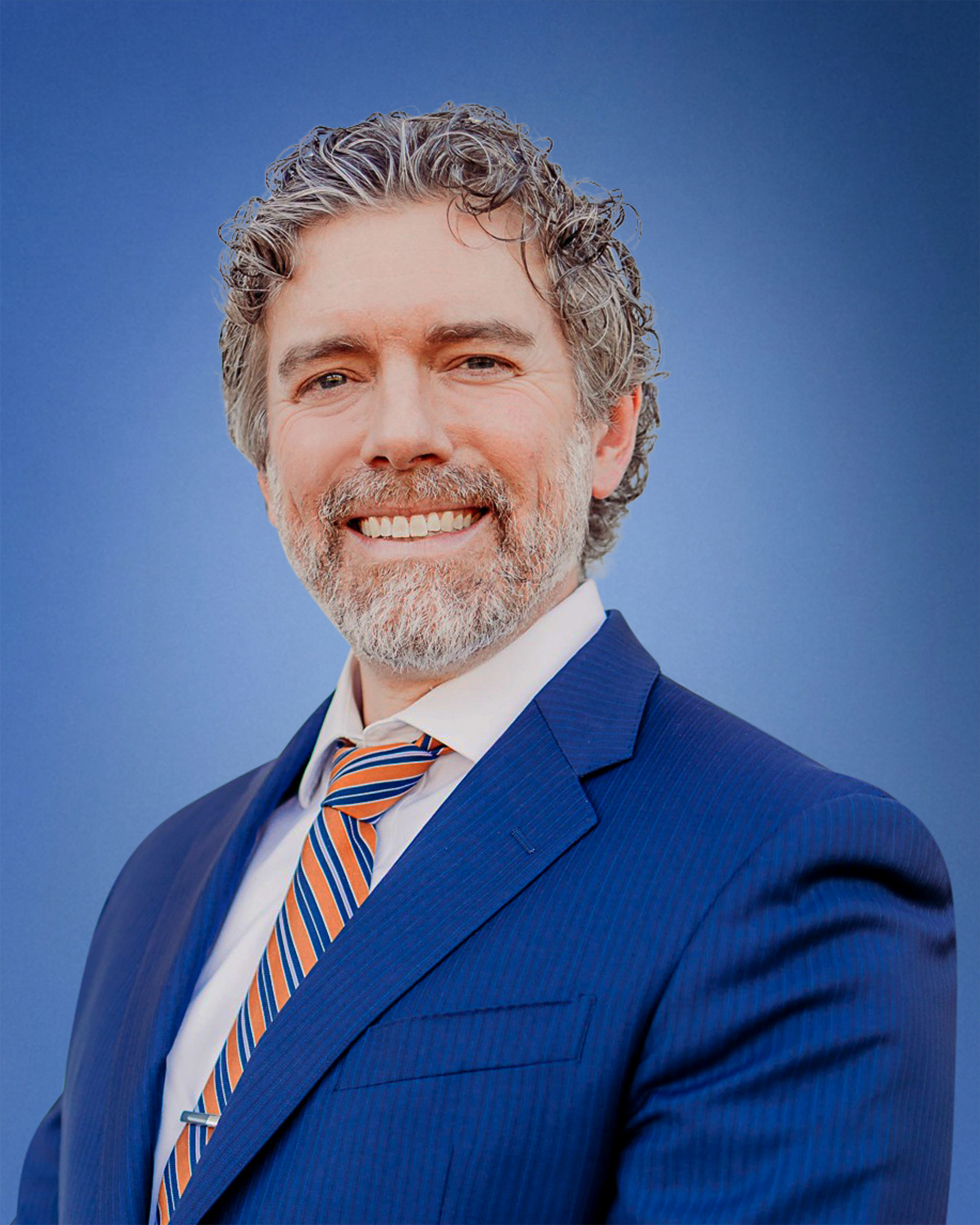 Smiling man in a blue suit with an orange striped tie against a blue gradient background (portrait)
